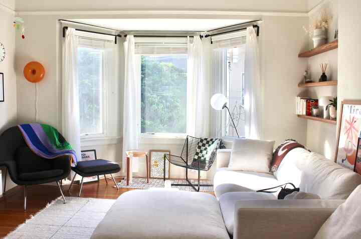 Bright white and natural-toned living room featuring a large sectional sofa and armchair around a bay window, creating a cozy atmosphere