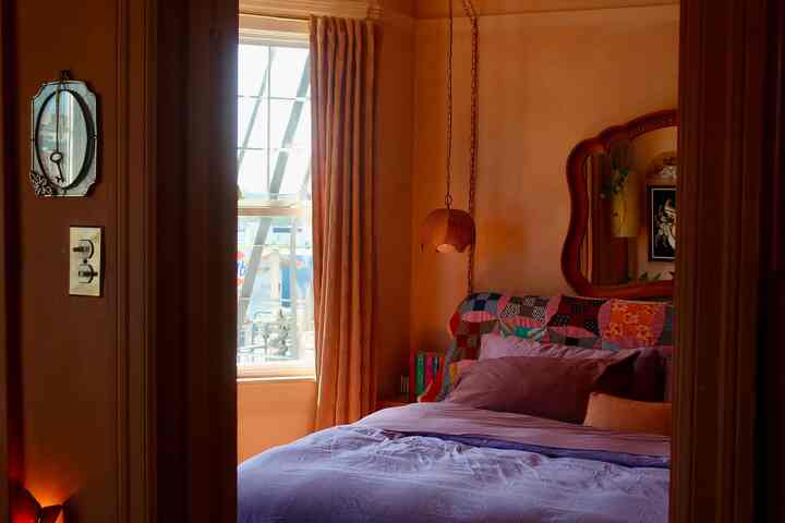 Warm light brown toned bedroom featuring a bohemian patchwork bedspread, curtains, pendant light, and wall mirror creating a cozy atmosphere