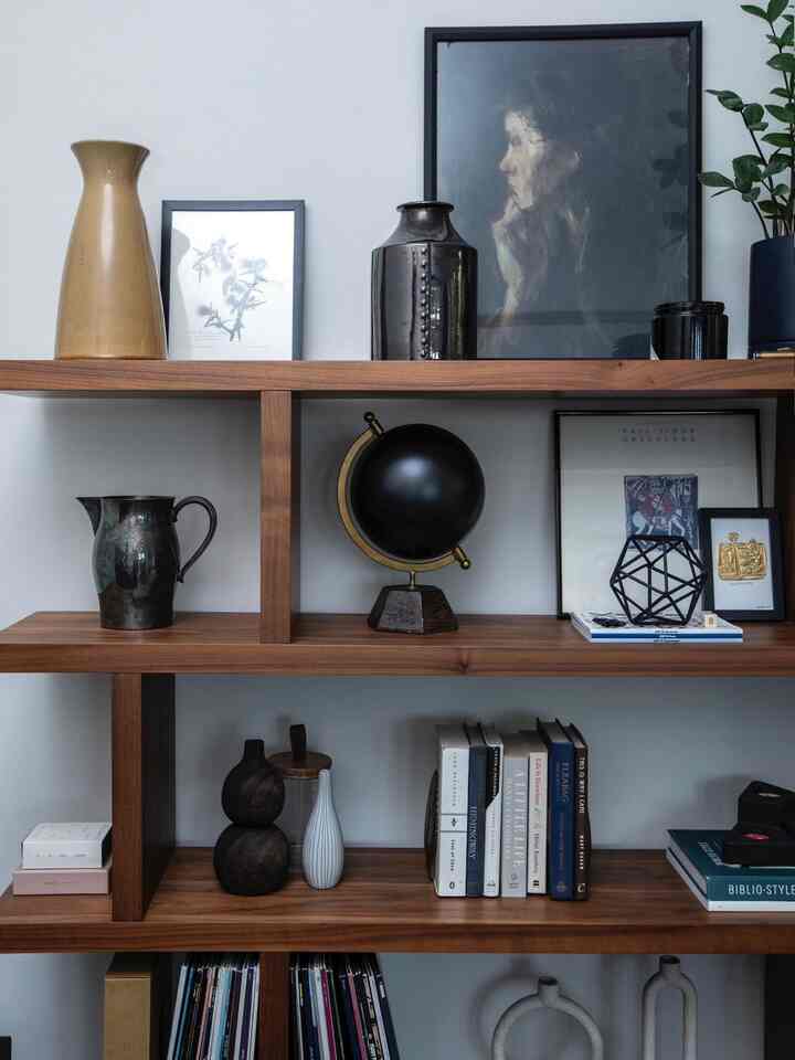 Dark wood tone bookshelf in a living room featuring various framed art and decorative objects in a clean mid-century modern style