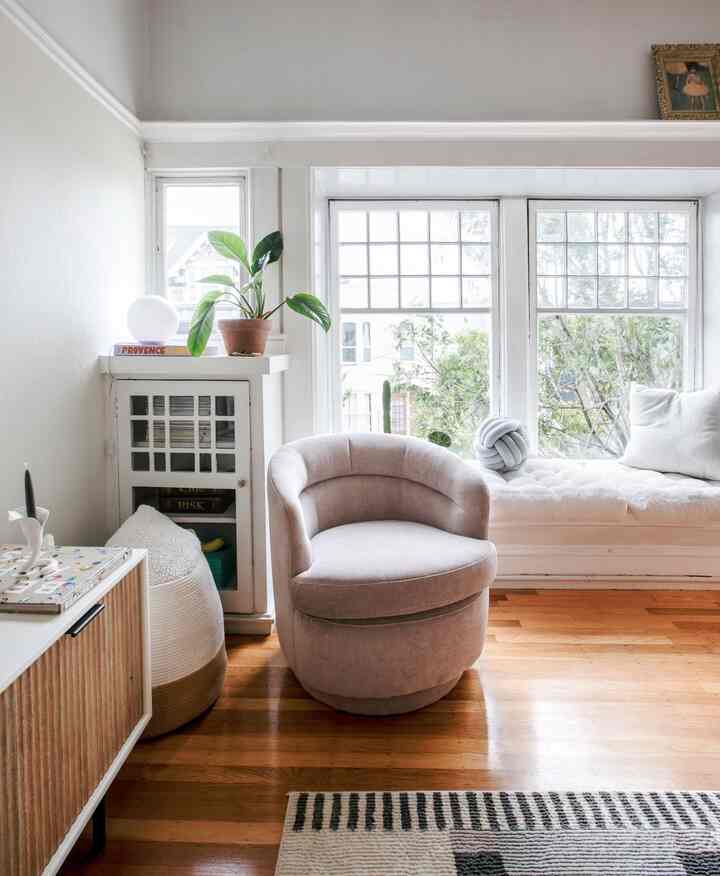 Bright white and wood-toned living room corner featuring beige armchair, cushions, and plants in a cozy setting