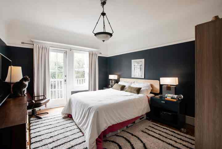 Modern bedroom in black and white tones featuring a central white bed with wooden frame and a cat sitting on the console table