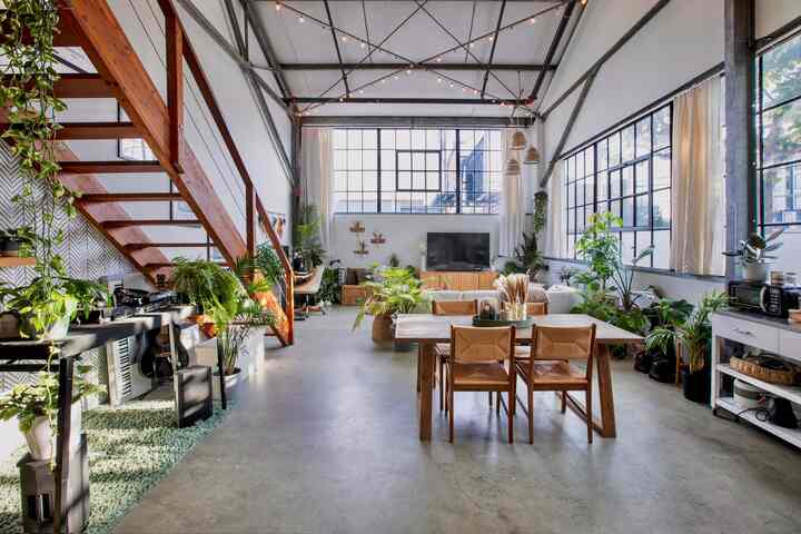 Natural tones and wood furnishings grace a boho living and dining room with abundant plants and tall ceilings, creating an airy atmosphere
