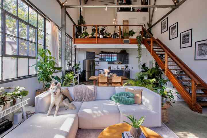 Bright white and warm wood-tone loft living room featuring large sectional sofa and abundant plants with cozy natural atmosphere