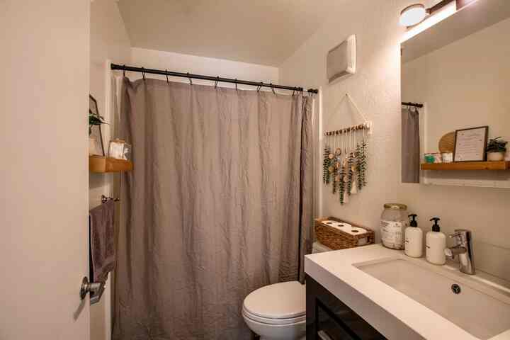 White and brown toned bathroom featuring a sink, toilet, and bohemian style wall decor creating a cozy atmosphere