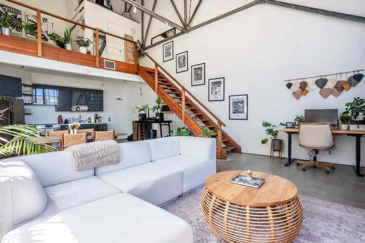 Natural toned wood and bohemian style living room featuring a white sofa, round ottoman, desk, and plants in a bright cozy space