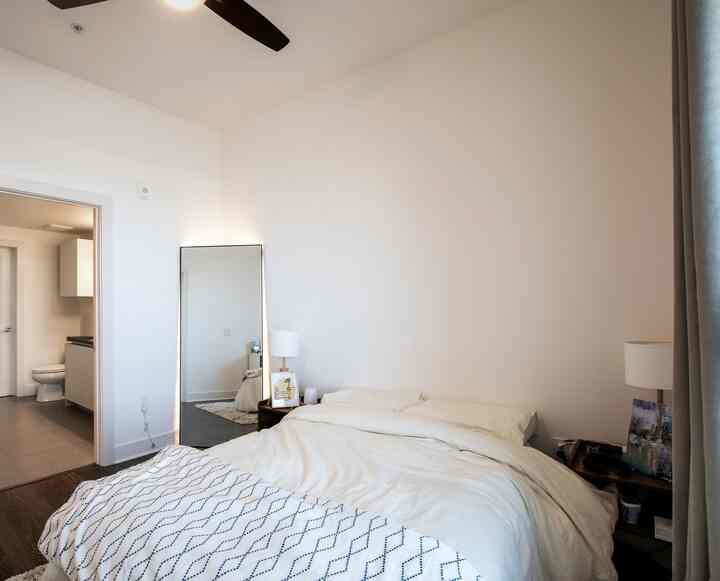 White-toned bedroom with queen-size bed, nightstands, and oversized mirror creating a simple and natural atmosphere