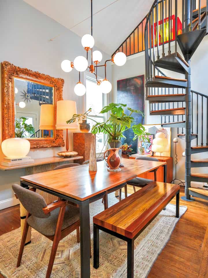 Bright wood tones and white walls in a dining room featuring a spiral staircase and vintage mirror, creating a classic ambiance
