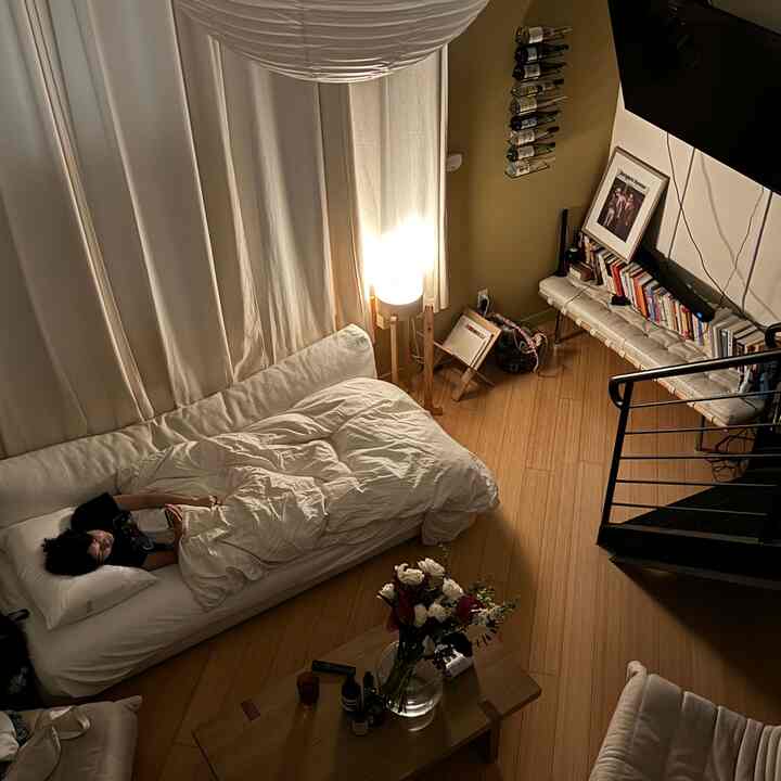 Natural wood flooring and white sofa bed in a Japandi style loft, featuring warm lighting and wall-mounted wine rack creating cozy atmosphere