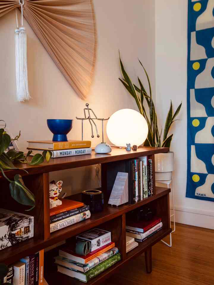 Warm brown wood-tone living room with mid-century modern bookshelf, round table lamp, and plants creating a cozy atmosphere
