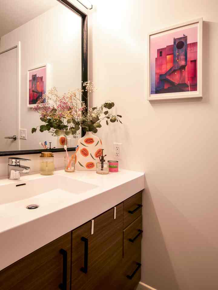 White and wood tone bathroom featuring a washbasin decorated with plants and framed artwork, creating a modern and tidy atmosphere