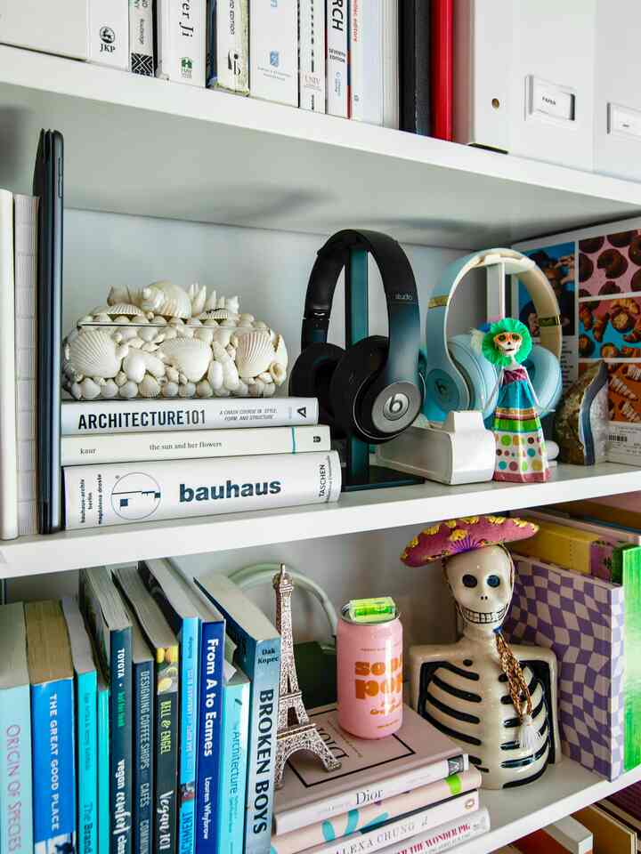 White-toned living room bookshelf featuring books, wireless headphones, and decorative accessories in a neat arrangement