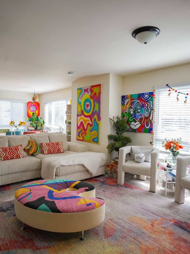 Bright modern living room with white walls and furniture, featuring colorful wall art and rug creating vibrant atmosphere