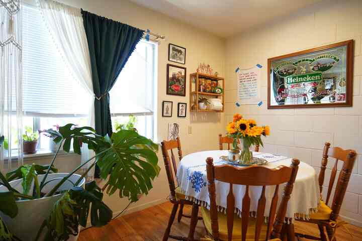 Natural color kitchen dining space with blue curtains, vintage wooden furniture, and sunflower centerpiece creating a cozy atmosphere