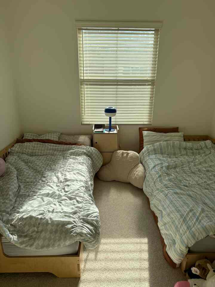 A beige and white toned kids' bedroom featuring two wooden beds and a central table lamp with a cozy atmosphere
