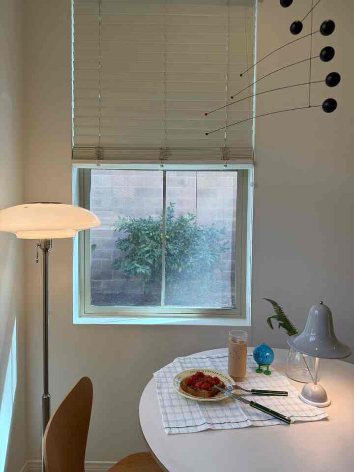 White and natural tone mid-century modern dining room featuring a round table, lamps, and window with blinds creating cozy ambiance