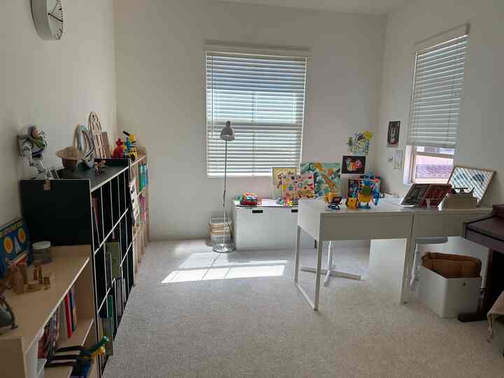 Bright and organized kids' room with white and natural tones, featuring two desks and multiple toy storage units for study and play