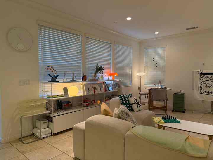 White and beige toned living room featuring sofa, coffee table, bookshelf, and lamps in a harmonious mid-century modern style interior