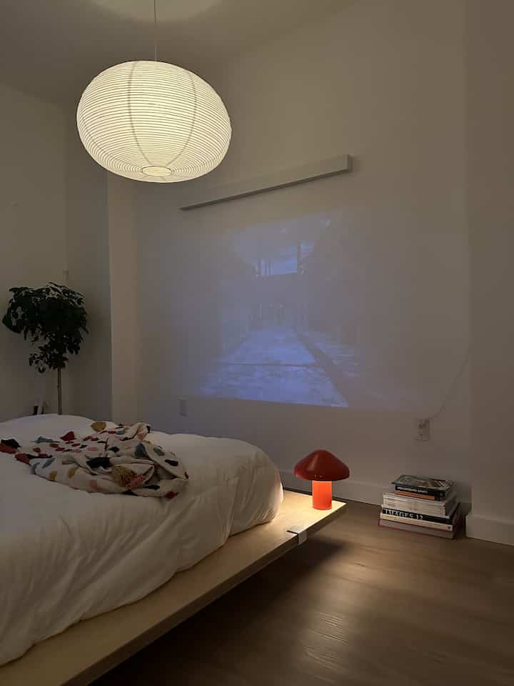 Natural and white toned bedroom featuring a wooden bed frame and a red mushroom-shaped table lamp, creating a cozy atmosphere