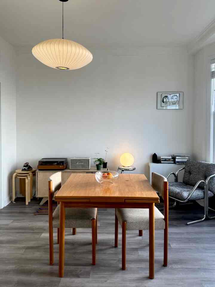 A white-walled natural mid-century modern dining room featuring a wooden dining table and pendant light