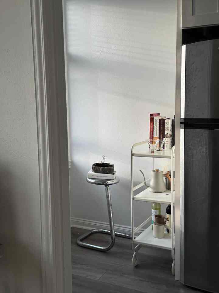 White and chrome-toned kitchen corner featuring a minimalist modern bar cart and chrome stool with natural light casting shadows