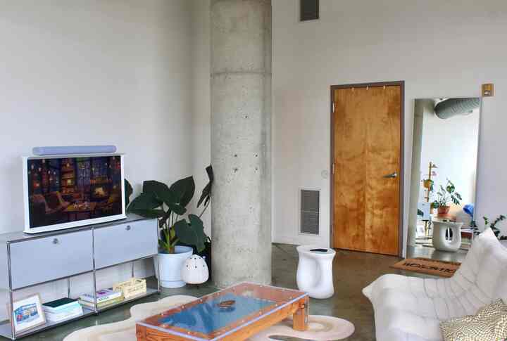 Bright wood-toned door, white walls, white sofa, glass-top wooden table, and plants arranged in a Scandinavian style living room