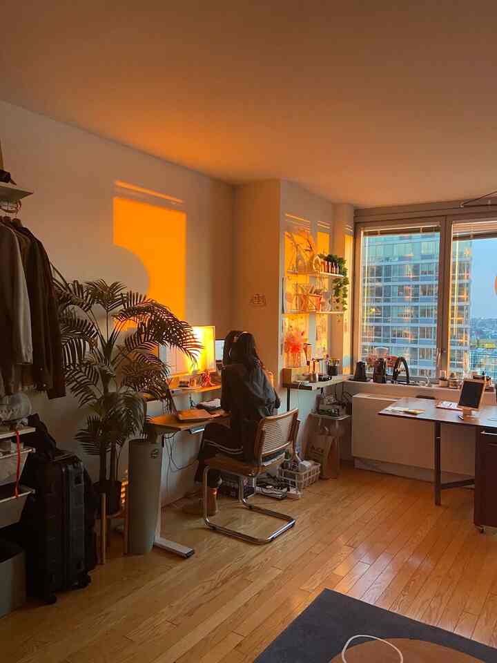 Warm ivory walls and wood-toned floor create a 1LDK home office and kitchen space featuring plants and large windows with cozy ambiance