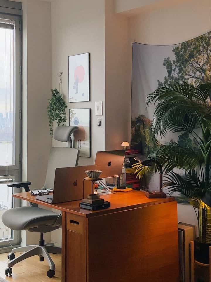 Warm wood tones and natural green plants define this mid-century modern home office featuring dual laptops and ergonomic chair with cozy vibes