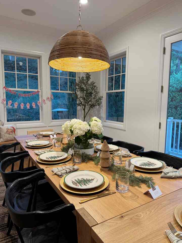 Wood tone and white dining room featuring a large dining table and black chairs set for a Christmas home party