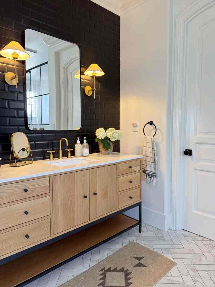 Modern natural bathroom featuring black tiled wall, wood-tone vanity with gold fixtures, and wall sconces