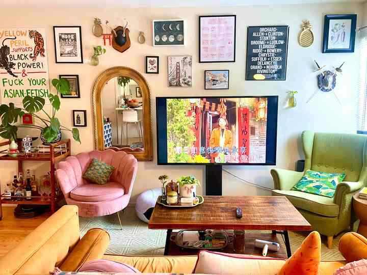Colorful maximalist living room with pink armchair and green wing chair, various framed wall art and decorations displayed