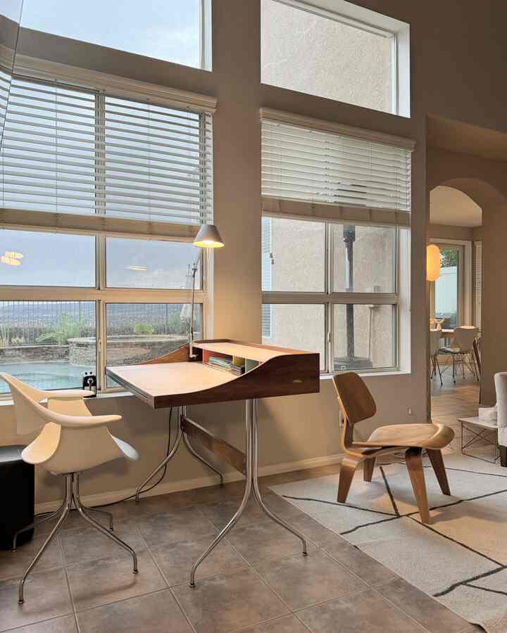 Bright toned mid-century modern home office featuring wooden desk and white chair near window with cozy atmosphere