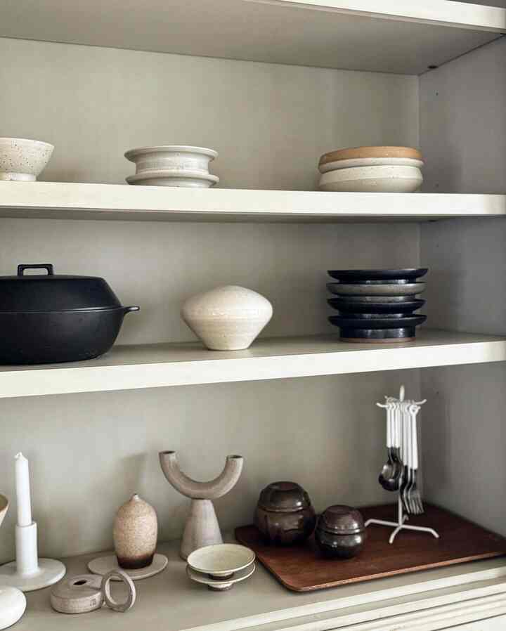 Natural beige and brown toned cabinet shelves featuring a pottery collection in a cozy space