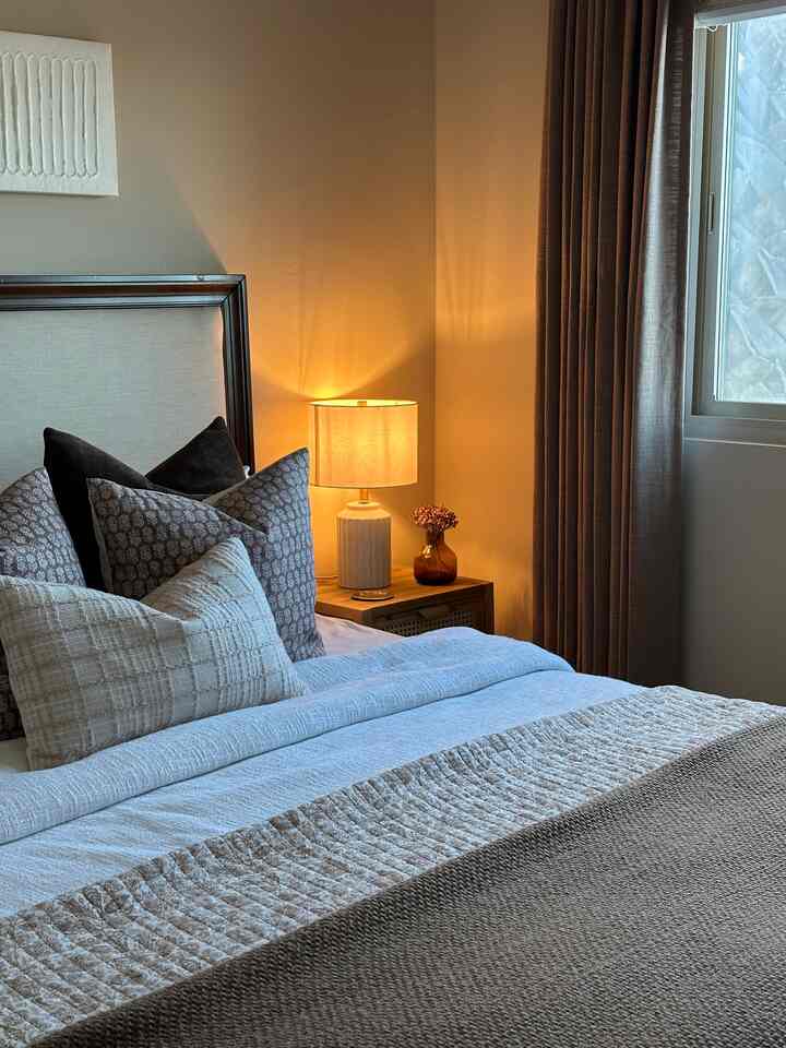 Natural beige-toned bedroom featuring cozy blanket and cushions with a ceramic table lamp, creating a warm and inviting atmosphere