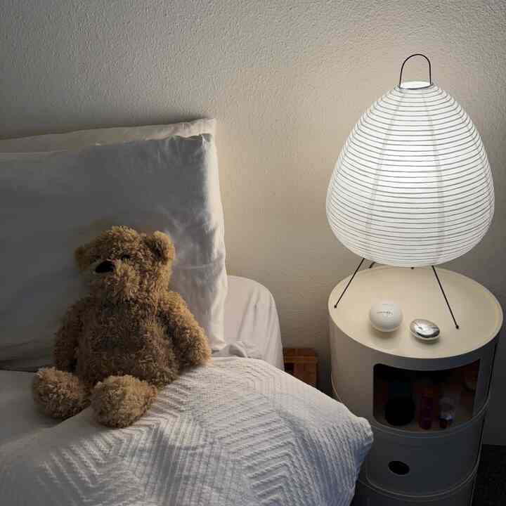 Natural-colored bedroom featuring a side table with an Akari lamp and a brown teddy bear, creating a cozy atmosphere