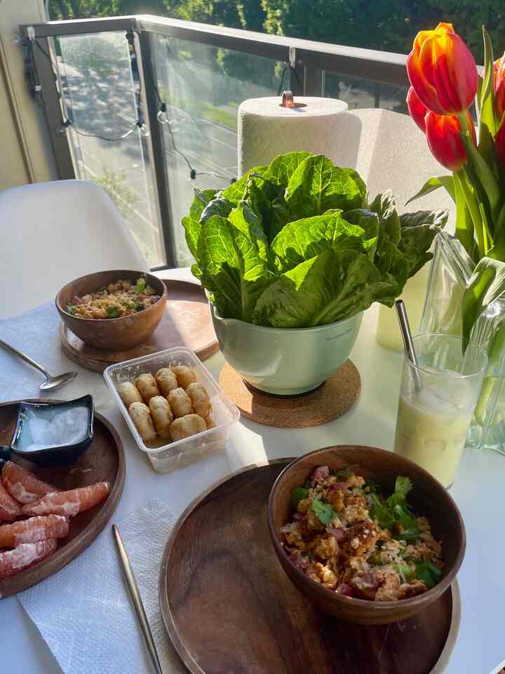 Sunlit balcony with a white table featuring natural green leaves and wooden bowls creating a relaxed outdoor dining spot