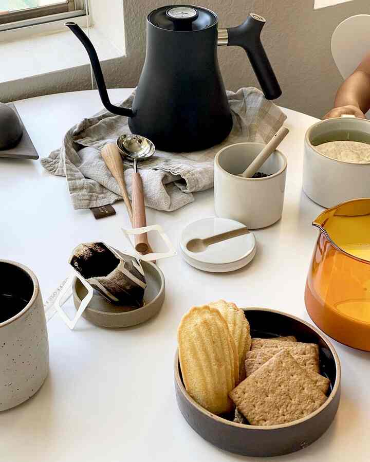 White table featuring natural-toned ceramics, black pour-over kettle, and dessert plate in a home cafe setting