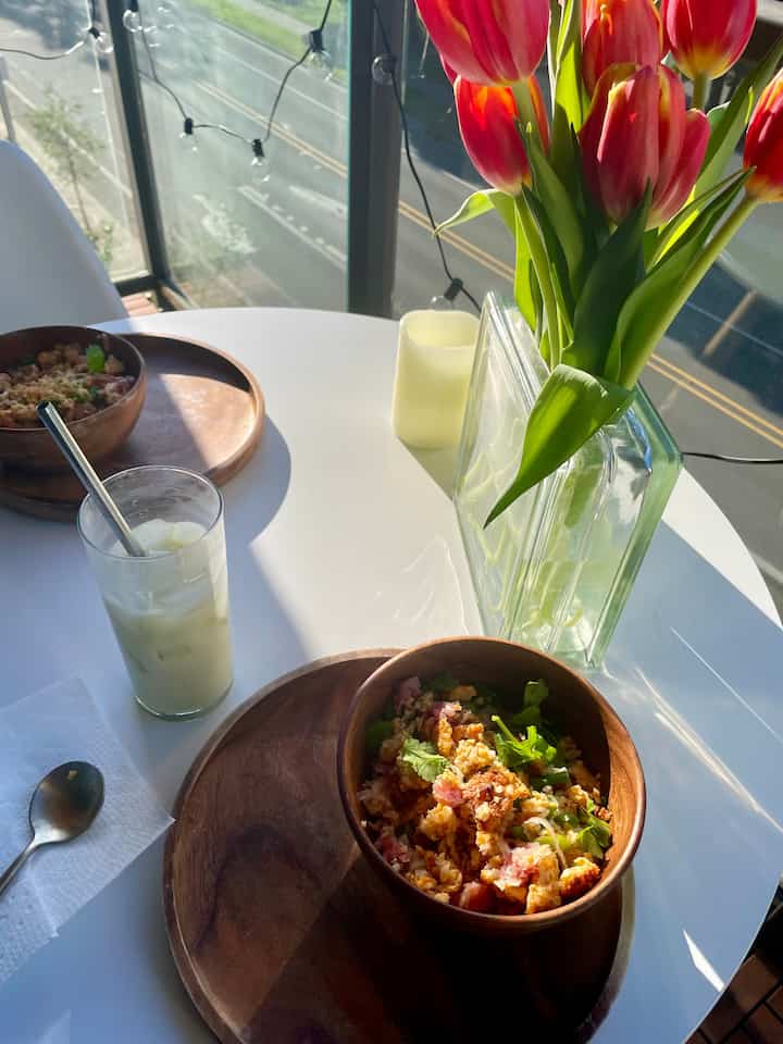 White and wood tone balcony dining space featuring wooden tableware and vase with flowers, creating a cozy home date atmosphere