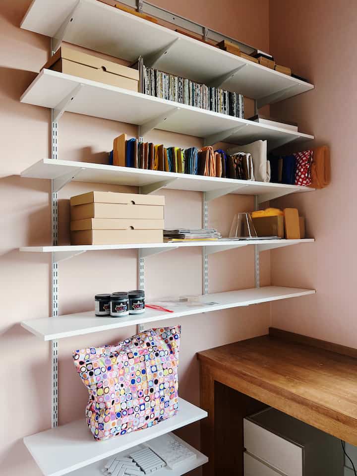 Cozy corner space with pink-toned walls, white shelves, and a wooden desk