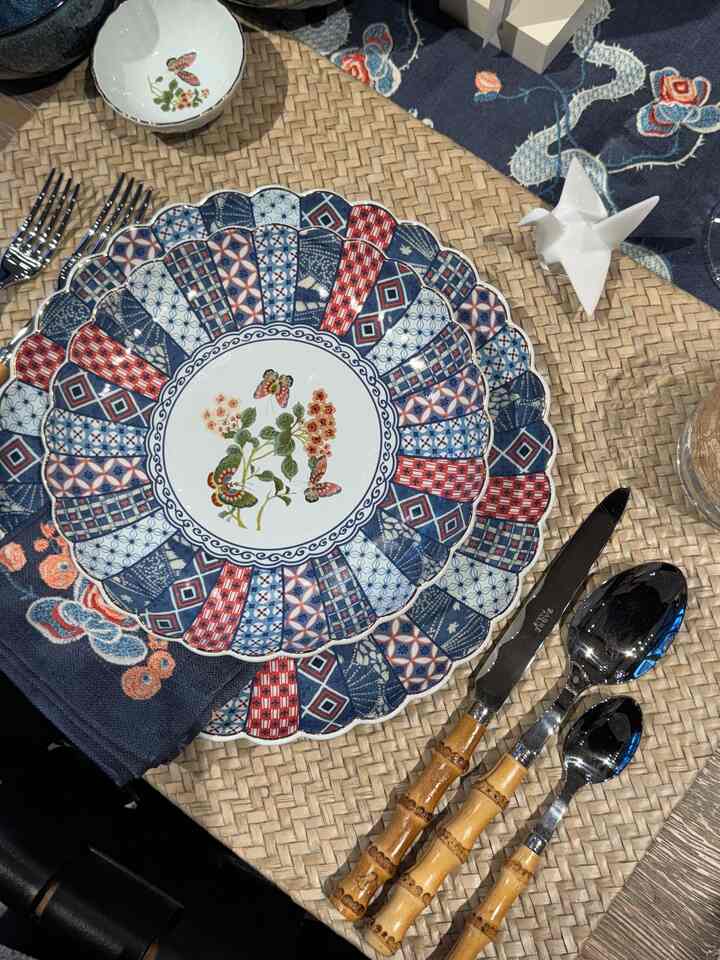 Beige woven placemat with blue and red patterned Japanese-style plates and bamboo-handled cutlery set arranged elegantly on table