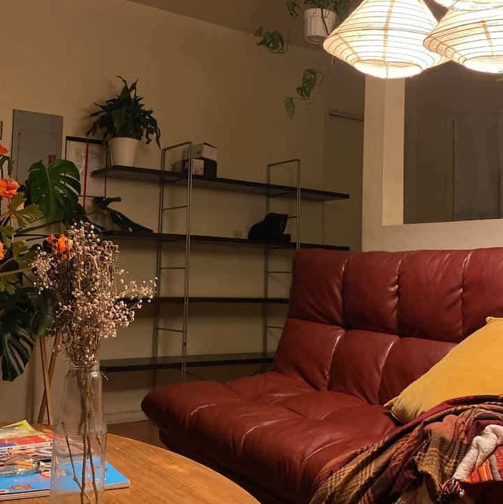 A warm natural-toned living room featuring a red leather sofa, round wooden coffee table, and plants creating a cozy atmosphere