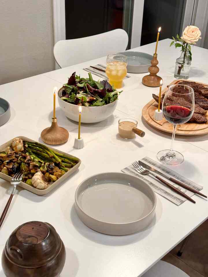 White dining table set with brown candle holders, plates, wine glasses, and salad bowl for a two-person Valentine's Day home date