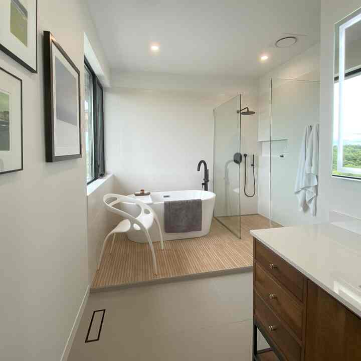 Modern bathroom in white and wood tones featuring a freestanding bathtub, glass shower booth, and wood floor platform