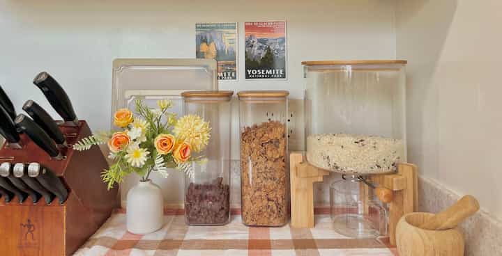 Beige and brown toned kitchen countertop featuring a wooden knife block, vase with flowers, and transparent airtight containers creating a cozy atmosphere
