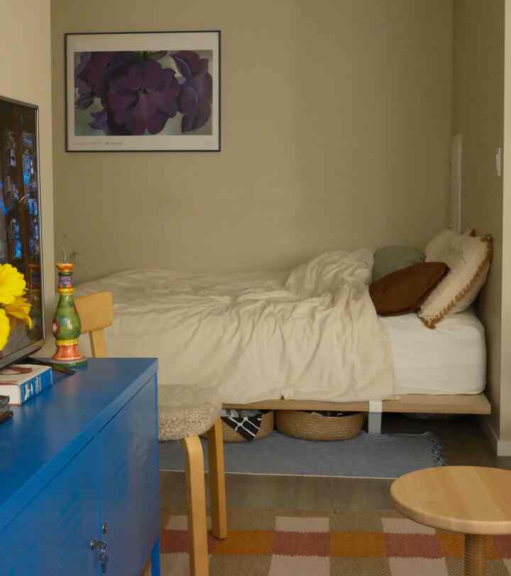Beige and blue toned studio apartment bedroom featuring a bed, a blue storage cabinet, and cozy natural wood furniture