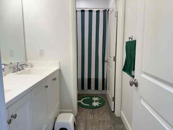Modern bathroom in white and green tones, featuring a striped shower curtain, green bath mat, and towel with a clean aesthetic