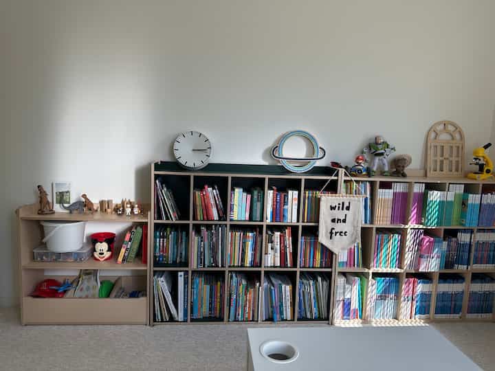 Natural kids' room with white walls and wood tone bookshelves, featuring a kids' desk, clock, and books in a cozy setting