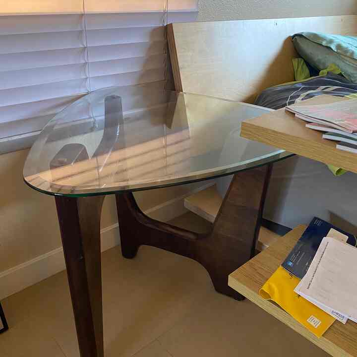 Warm natural wood tones feature a simple side table with glass top alongside a workspace in a cozy room