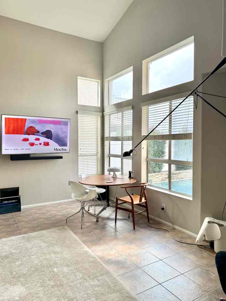 Bright white-toned living room with large windows featuring a round mid-century modern dining table and wooden armchair in a warm atmosphere