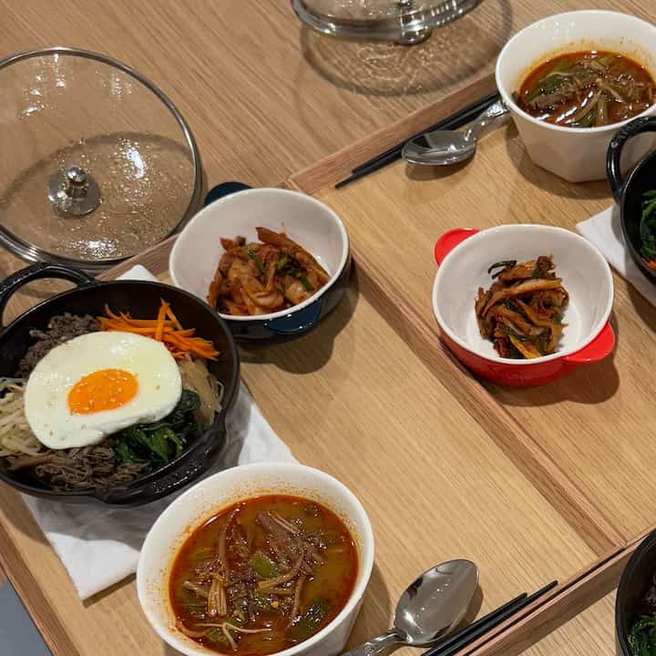 Wood tone dining table featuring Staub pot and white bowls arranged as a Korean bibimbap meal setting