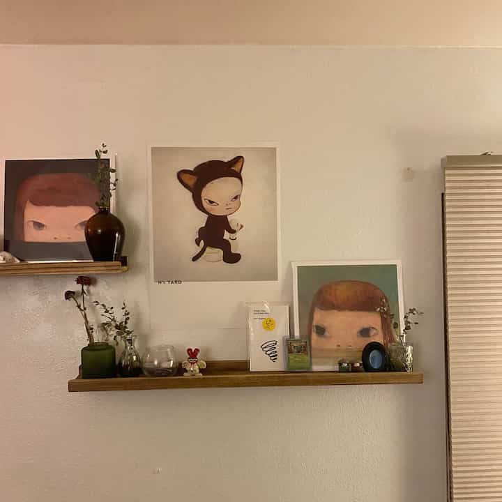 Natural-toned wall with wooden shelves, vases, and art posters creating a cozy objet space